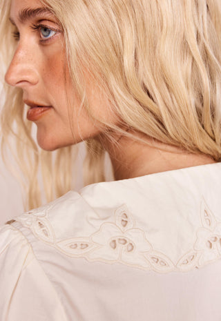 close-up-side-profile-of-a-blonde-woman-wearing-a-cream-colored-blouse-with-delicate-eyelet-embroidery-around-the-collar