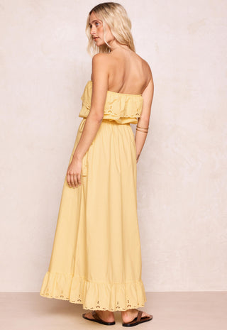a-woman-modeling-a-pale-yellow-strapless-maxi-dress-with-ruffle-details-shown-from-the-back-against-a-textured-beige-wall