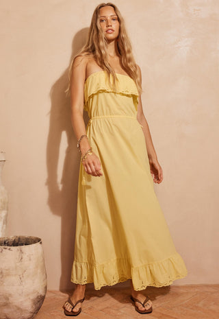 a-woman-modeling-a-strapless-yellow-maxi-dress-with-ruffle-details-standing-against-a-textured-beige-wall
