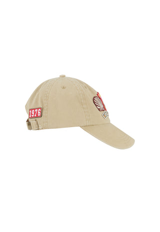 A beige baseball cap with a red and white '1976' patch on the side and a red and white crest patch on the front, shown against a plain white background.