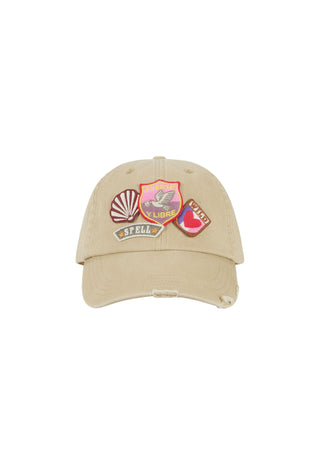 A beige distressed baseball cap featuring three colorful embroidered patches on the front, set against a plain white background.
