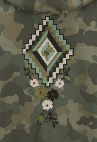 Close-up of a camouflage hoodie featuring a large geometric diamond patch in black, white, and teal, with embroidered white and black flowers below.