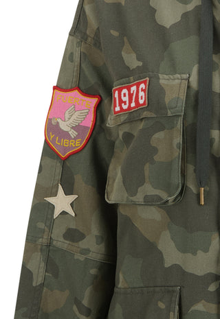 Close-up of a camouflage jacket with a pink and yellow patch, a red '1976' patch, and a white star patch on the sleeve.